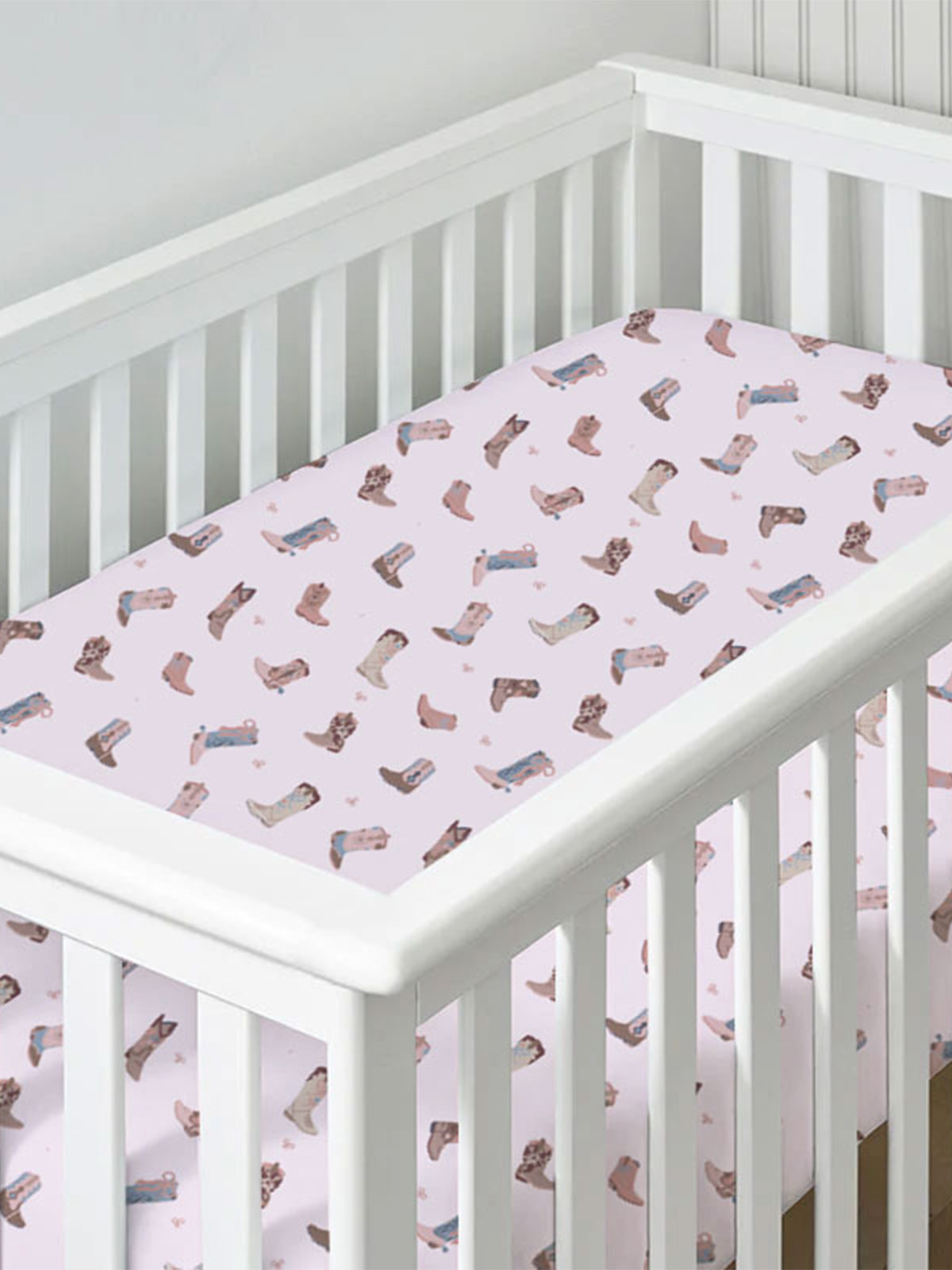 Crib with a soft pink sheet featuring an adorable pattern of boots and flowers.