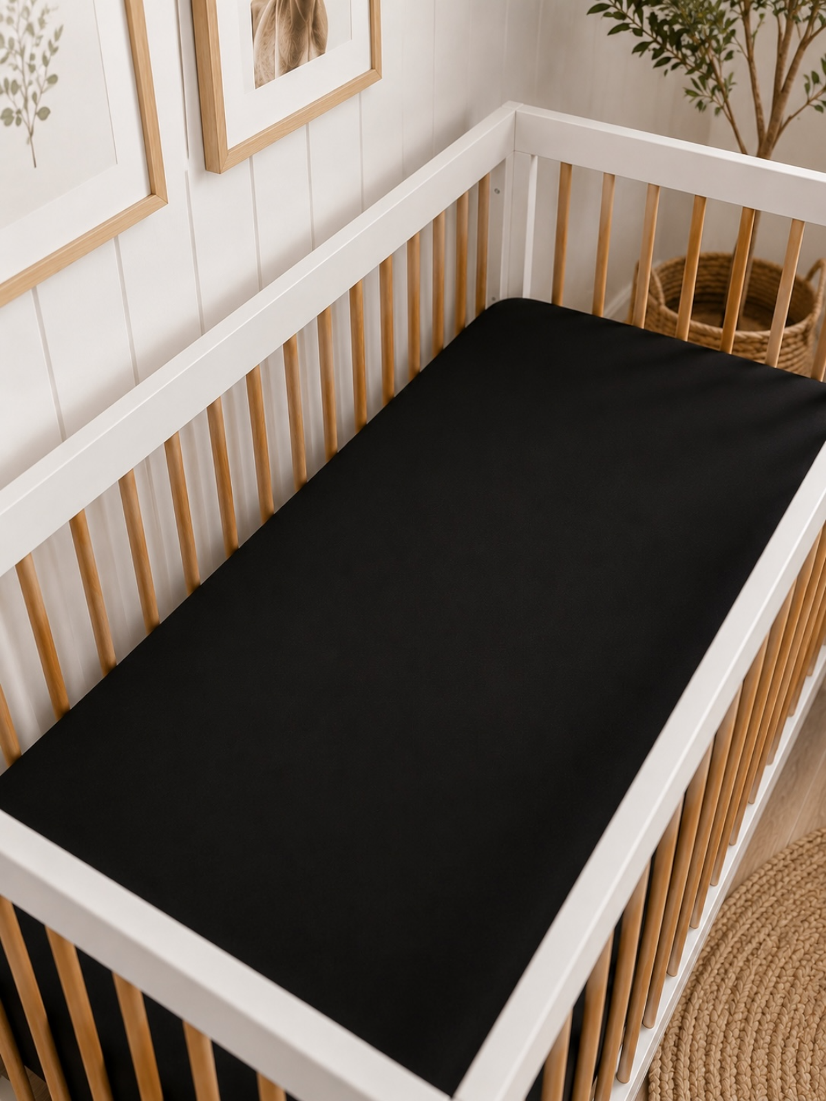 Black crib mattress on a white wooden crib in a stylish nursery with framed botanical art.