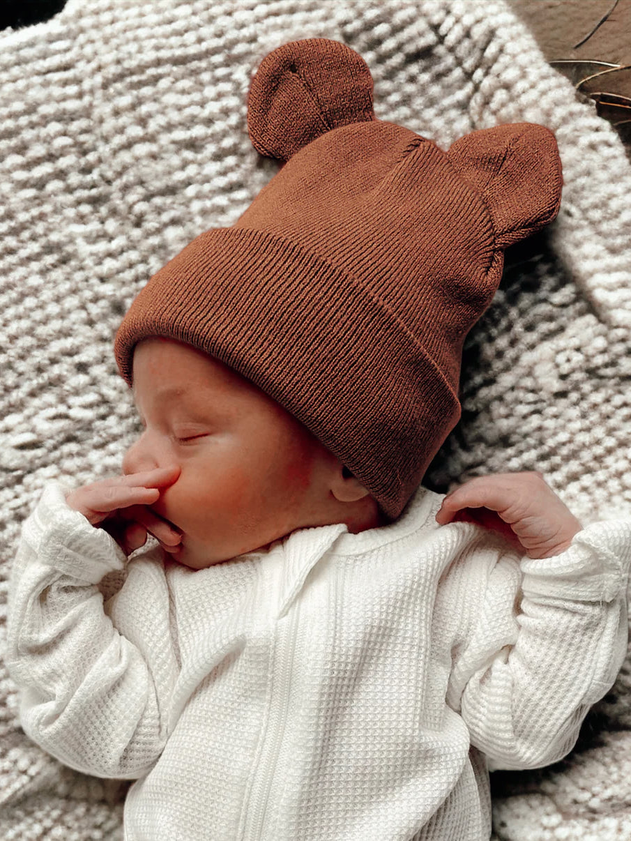 Newborn baby sleeping in a bear-ear hat, nestled in a cozy blanket, with a peaceful expression.