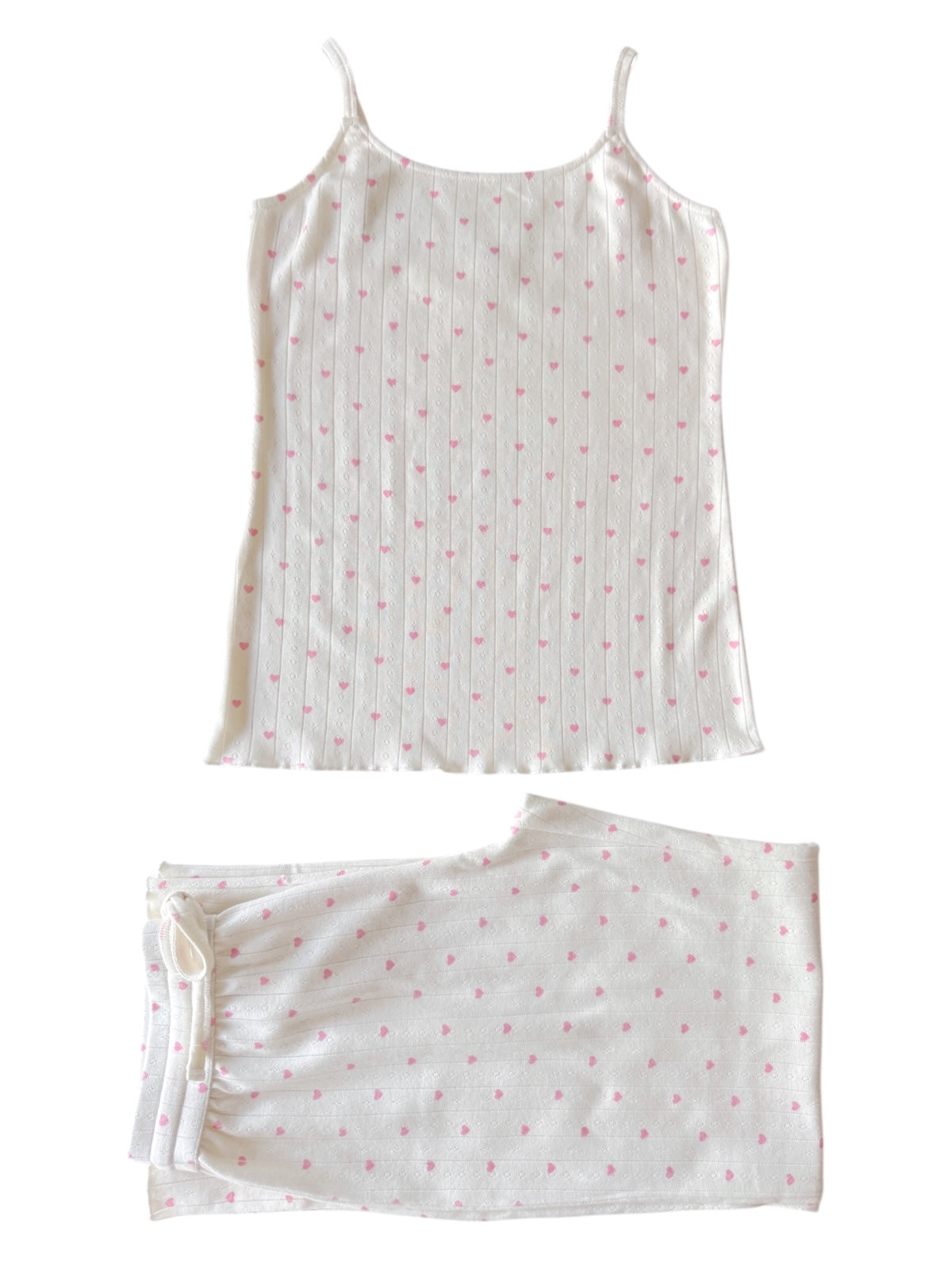 White pajama set with pink heart patterns, featuring a camisole top and matching pants laid flat.