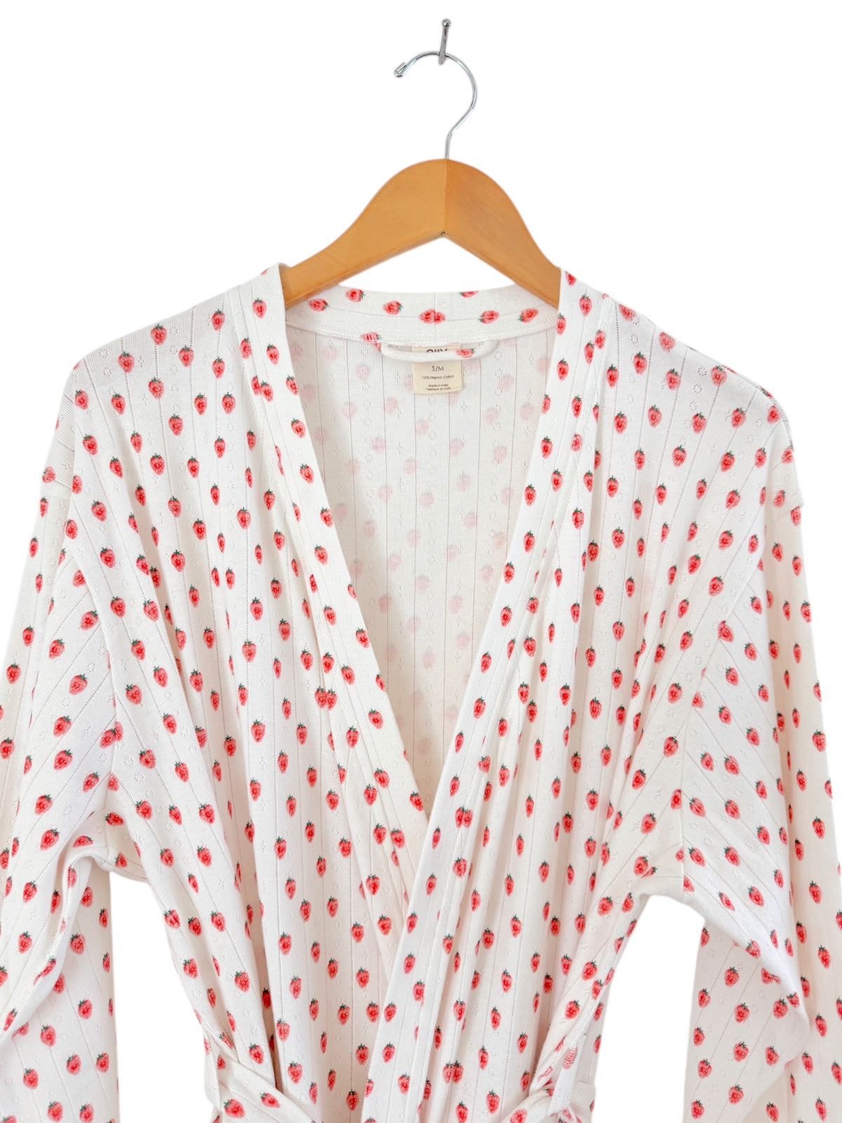 White robe covered in red strawberries, hanging on a wooden hanger against a plain background.