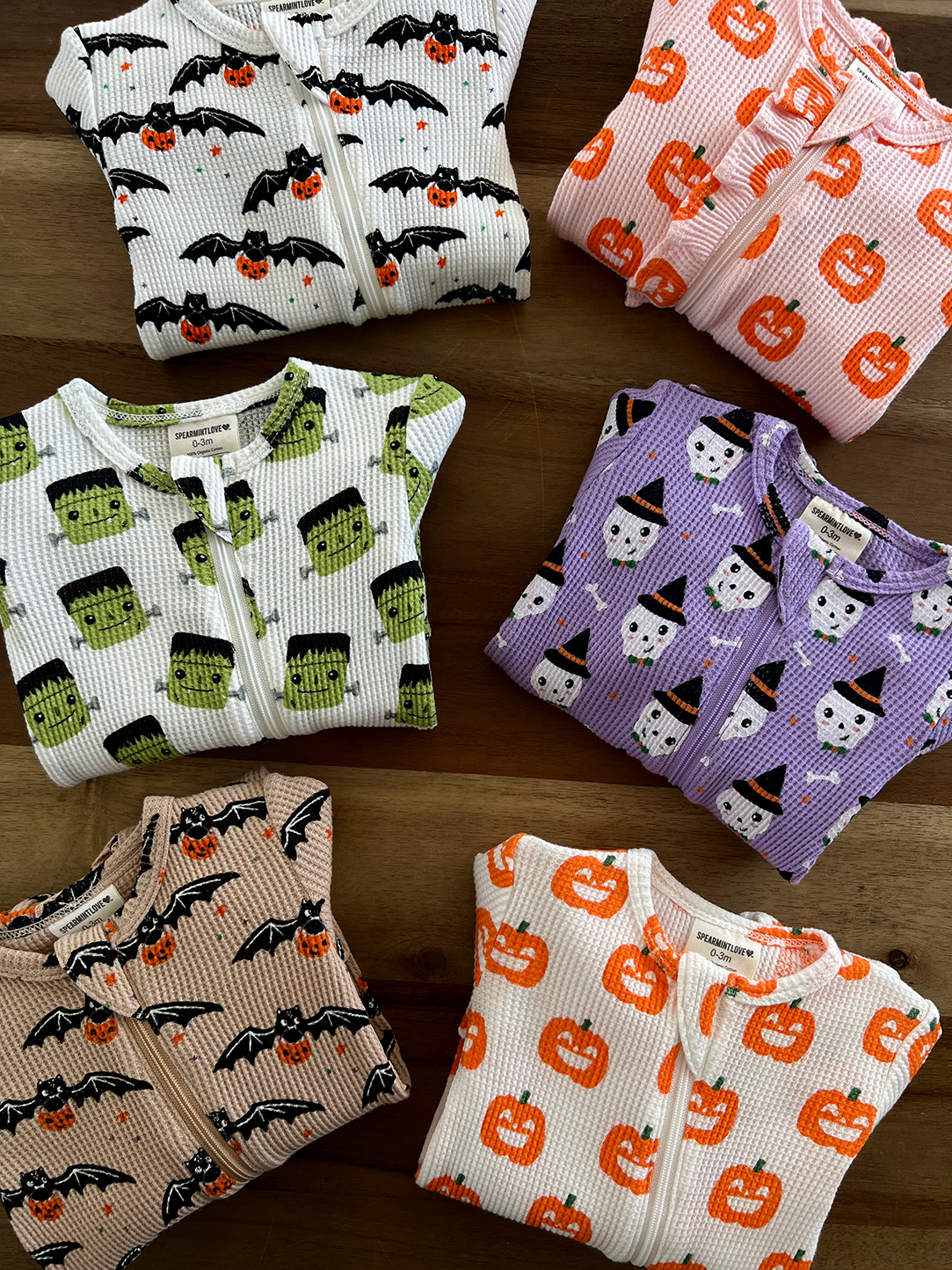 A collection of playful Halloween-themed onesies featuring bats, pumpkins, ghosts, and Frankenstein designs.