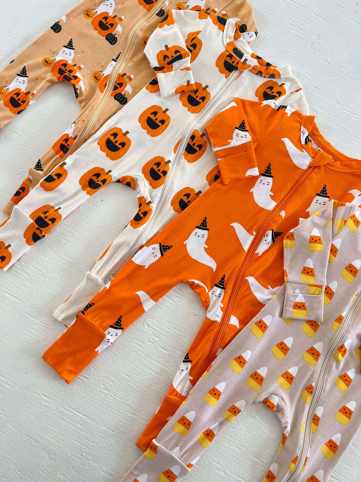 Four Halloween-themed baby onesies featuring pumpkins, ghosts, and candy corn patterns on a light background.