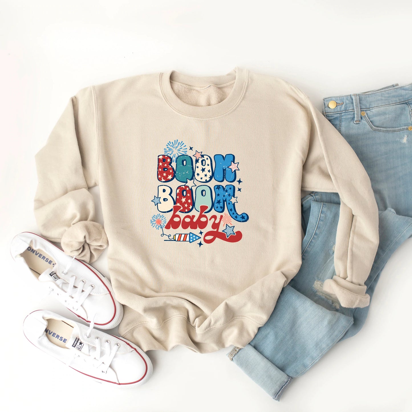 Beige sweatshirt with "Boom Boom Baby" design, paired with light jeans and white sneakers. Ideal for casual wear.