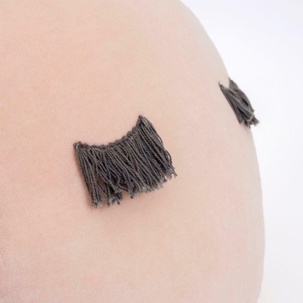 Close-up of a soft, round pillow featuring decorative dark fringe accents on a light background.
