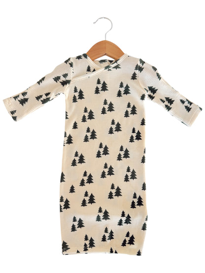 Long-sleeve baby outfit with a cream background and black tree patterns, hanging on a wooden hanger.