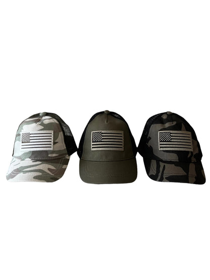 Three caps displaying American flags: one in camo, one in olive green, and one in black camo.
