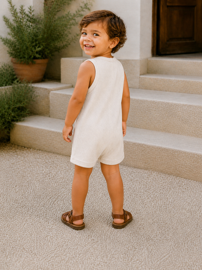 Smiling young child in a beige outfit stands on stairs, surrounded by greenery, looking back at the camera.