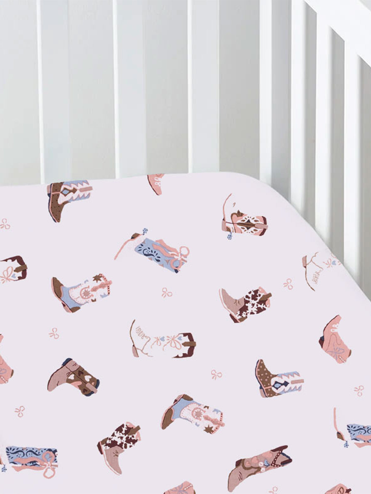 Cotton crib sheet with pink background and colorful cowboy boot patterns.