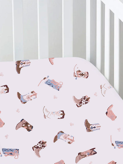 Cotton crib sheet with pink background and colorful cowboy boot patterns.
