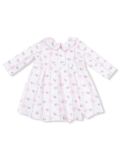 White dress with pink floral and bow print, featuring long sleeves and a rounded collar.