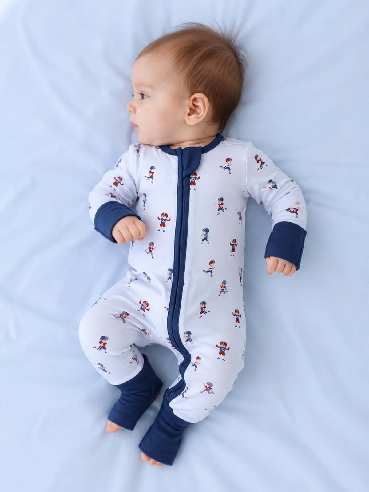 Baby in a playful onesie with colorful patterns, lying on a soft blue surface.