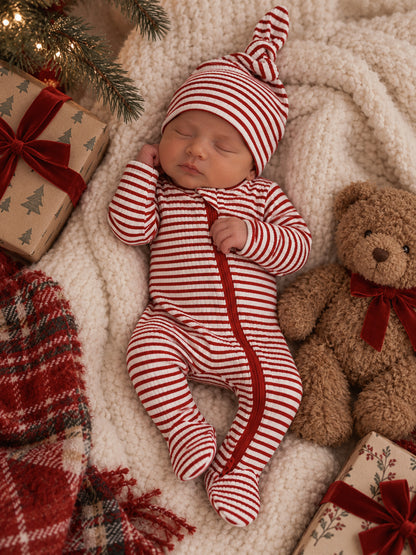 Newborn sleeping in striped red and white outfit, surrounded by gifts and a teddy bear on soft, cozy blanket.