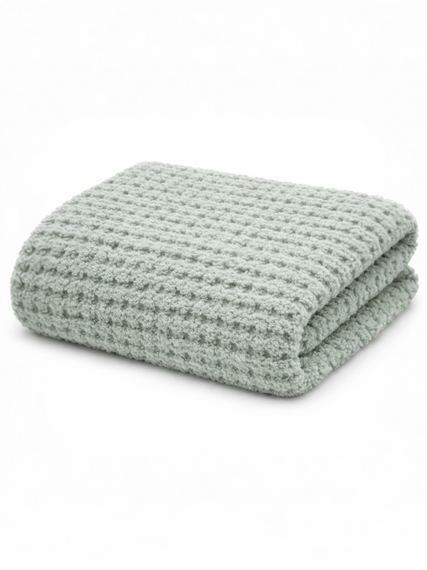 Soft green blanket with a textured, woven pattern, neatly folded on a light background.
