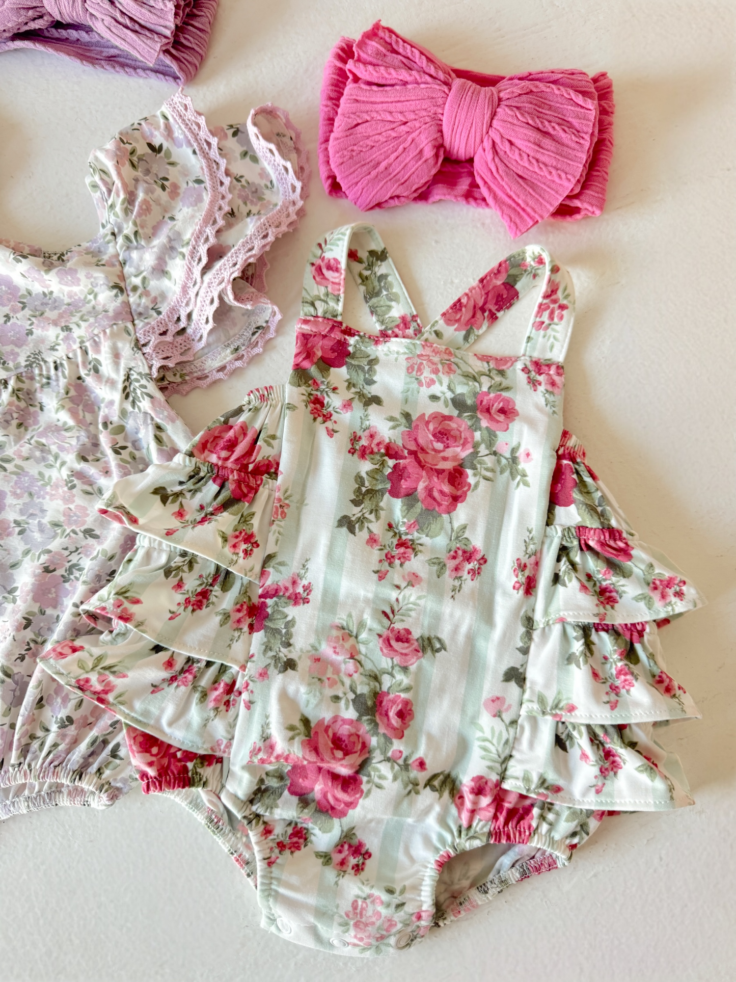 Floral baby romper with ruffled sleeves, paired with a pink bow headband and a second floral outfit.