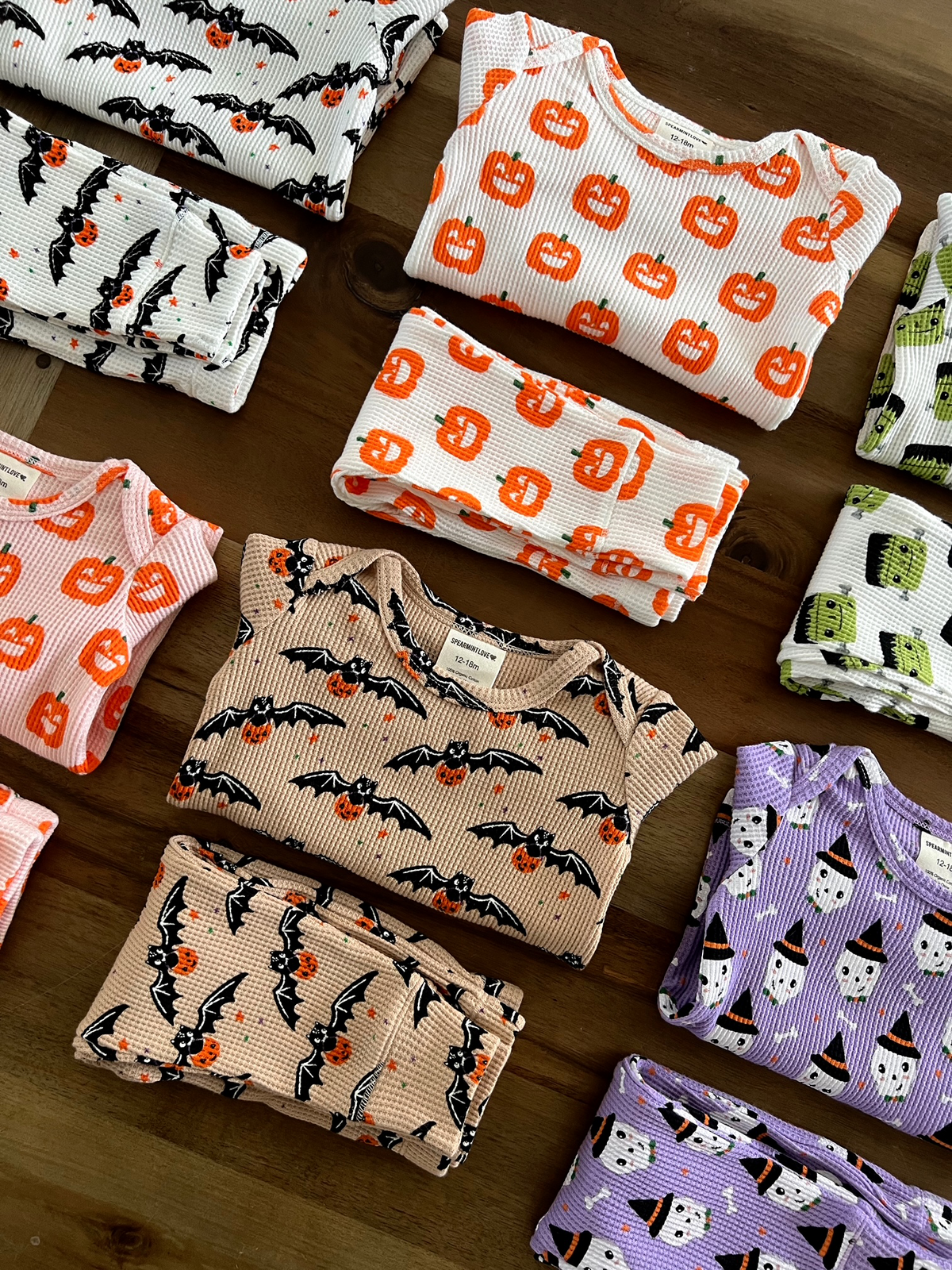 Colorful Halloween-themed children’s pajamas with bats, pumpkins, and ghosts arranged neatly on a wooden surface.