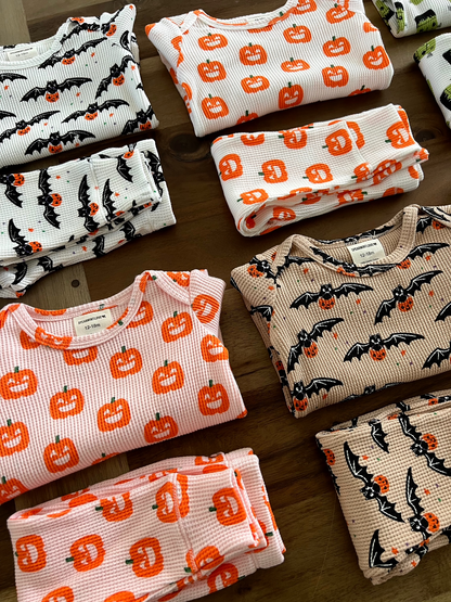 Folded children's pajamas featuring pumpkin and bat designs in various colors on a wooden surface.