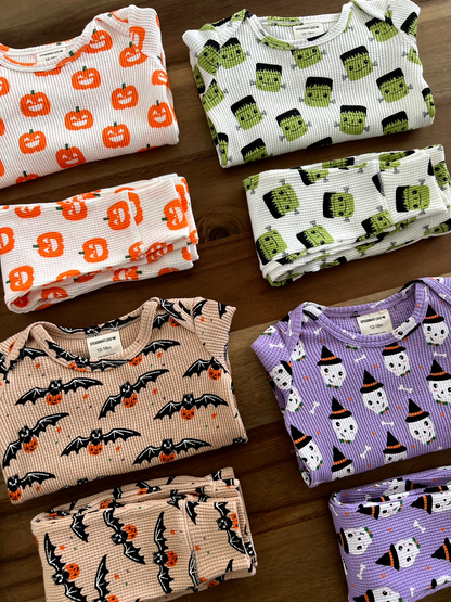 Colorful Halloween-themed infant clothing featuring pumpkins, bats, and ghosts, neatly folded on a wooden surface.
