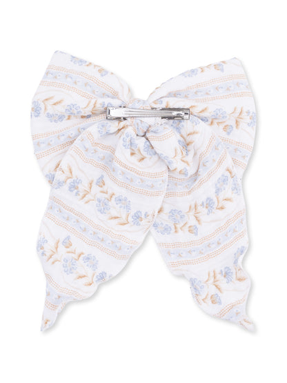 White fabric bow with light blue flowers and stripes, attached with a silver clip.