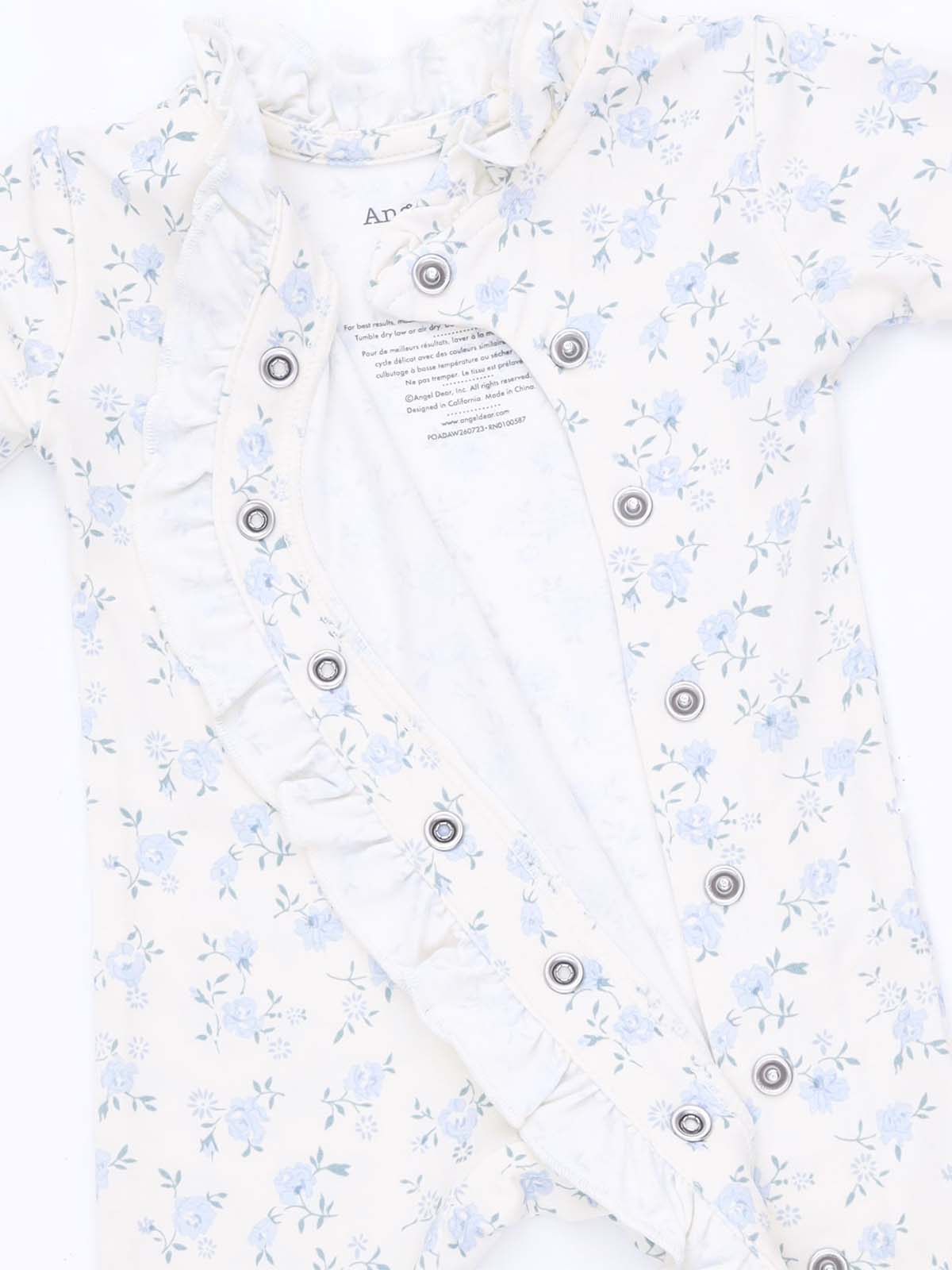 Floral baby onesie in cream with ruffle detailing and snap buttons, partially opened to show the inner lining.