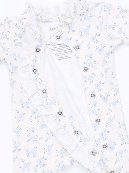 Floral baby onesie in cream with ruffle detailing and snap buttons, partially opened to show the inner lining.