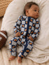 Baby in blue football-patterned onesie, lying on a soft blanket with a football nearby.