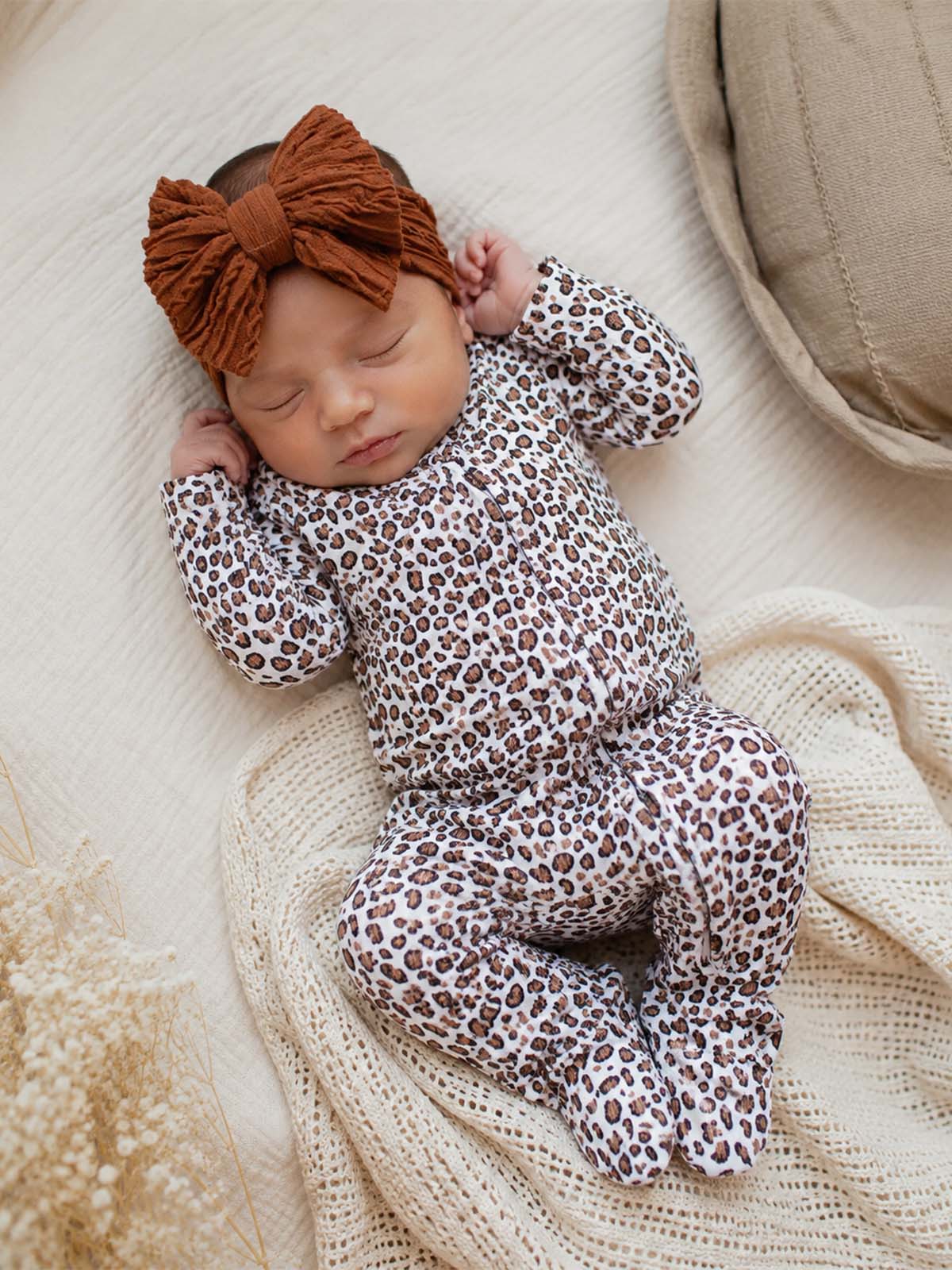 Baby sleeping on a cozy blanket, wearing a leopard-print outfit and a rust-colored bow headband.