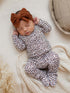Baby sleeping on a cozy blanket, wearing a leopard-print outfit and a rust-colored bow headband.