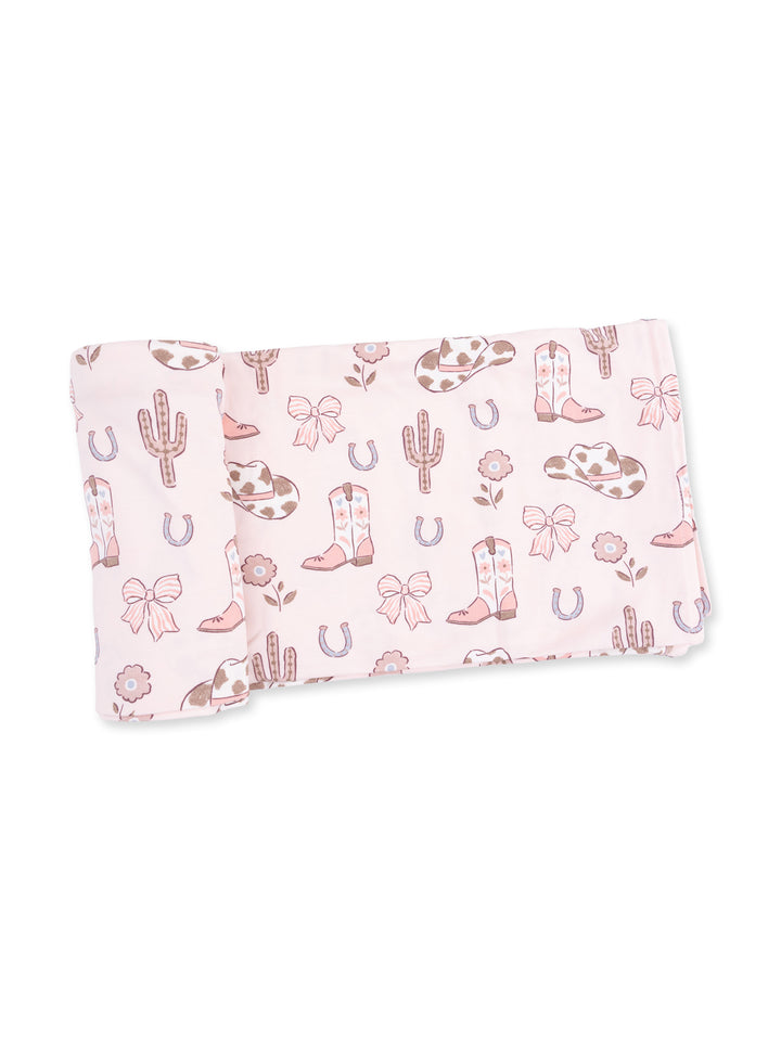Light pink fabric featuring a whimsical pattern of cacti, cowboy boots, bows, and horseshoes.