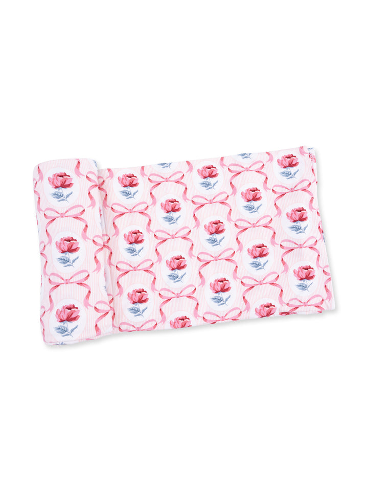 Rolled fabric featuring a pink floral pattern with ribbons on a white background.