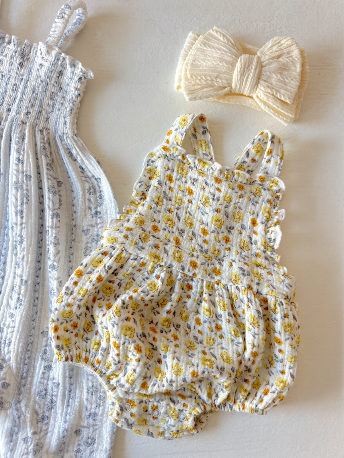 Floral baby romper and a cream bow headband on a light background.
