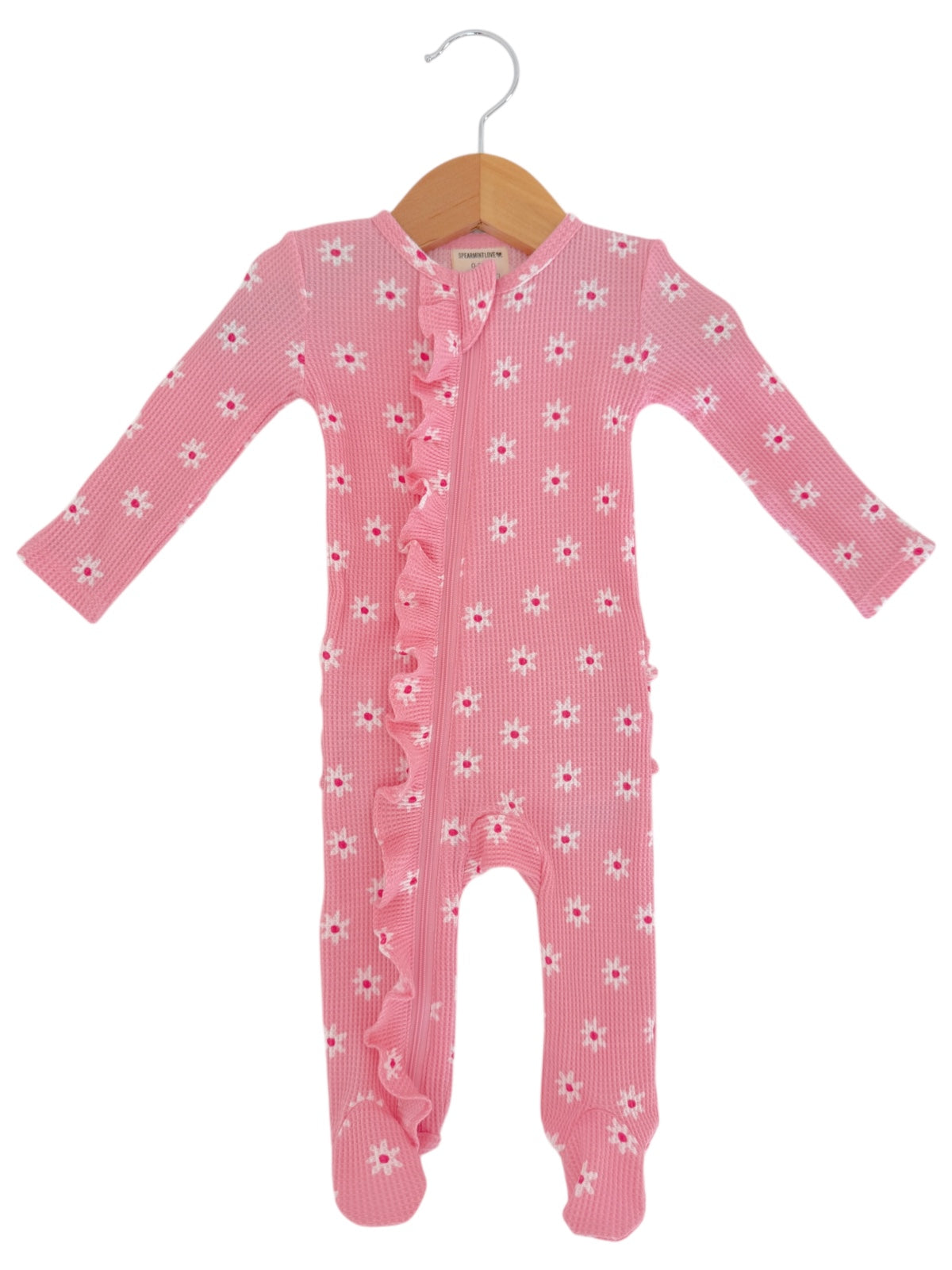 Pink baby onesie with white flowers and ruffles, hanging on a wooden hanger.