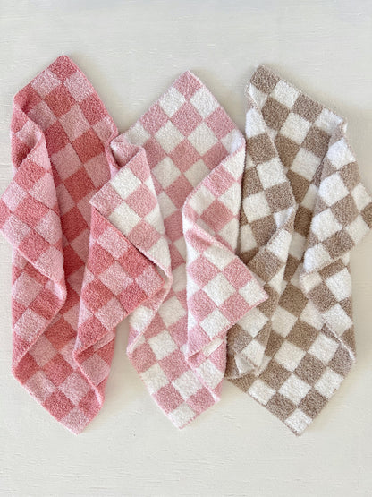 Three folded checkered towels in pink, white, and brown on a light background.