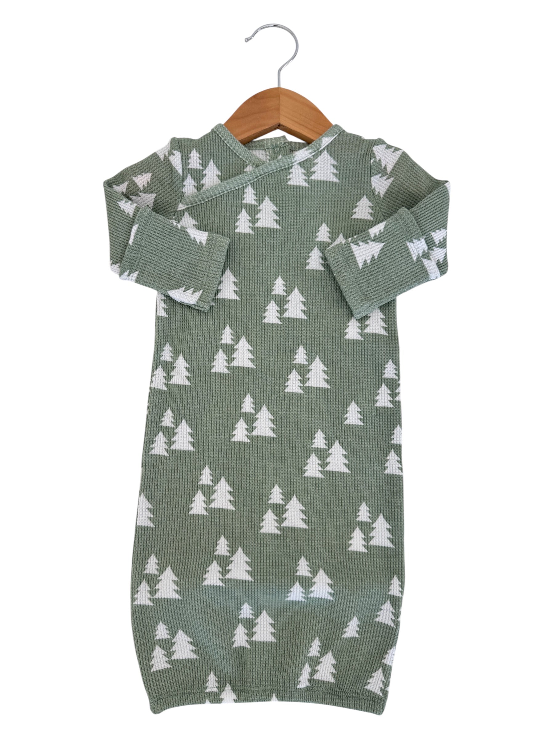 Green infant outfit with white tree pattern, hanging on a wooden hanger against a white background.