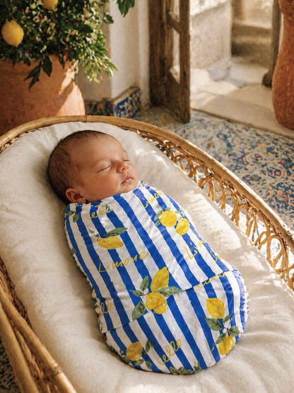 Sleepy baby swaddled in a blue and white striped blanket with lemon patterns, resting in a cozy basket.