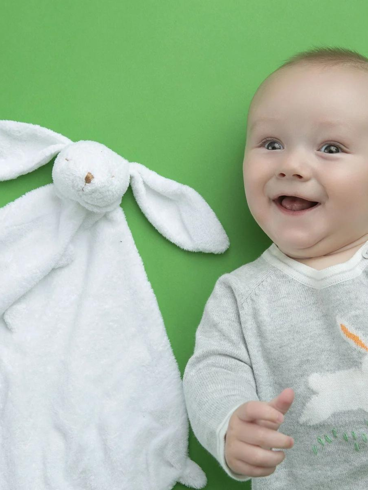 Smiling baby beside a white bunny blanket on a vibrant green background.