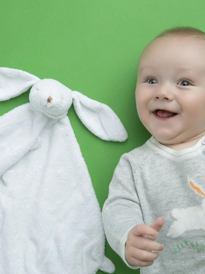 Smiling baby beside a white bunny blanket on a vibrant green background.