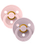 Two colorful pacifiers in soft pink and lavender with a round shield and a golden nipple.