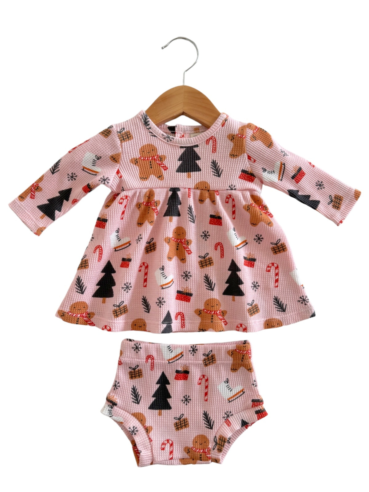 Pink toddler dress with gingerbread and Christmas patterns, paired with matching bloomers, hanging on a wooden hanger.