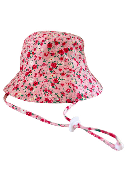Floral pink bucket hat with a chin strap, featuring small red and green flowers throughout the fabric.