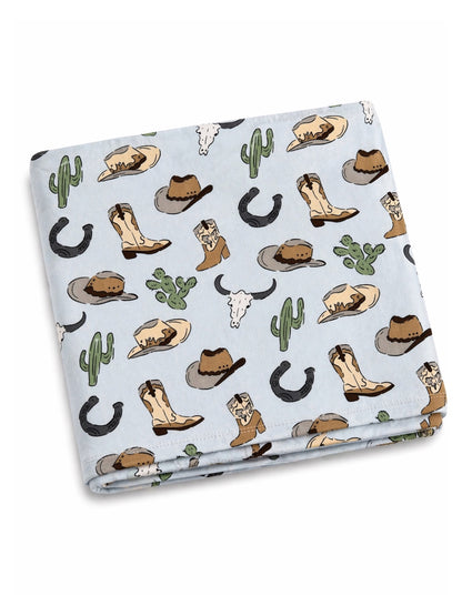 Light blue blanket with cowboy-themed patterns, featuring boots, hats, cacti, and horseshoes.