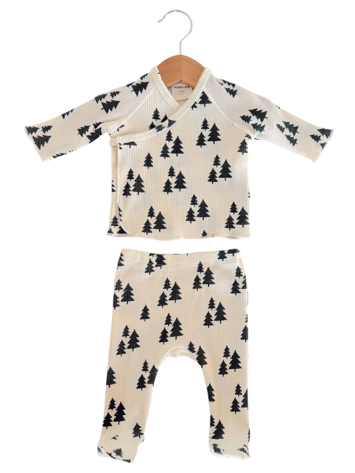 Cream outfit set for toddlers featuring black tree patterns, displayed on a wooden hanger.