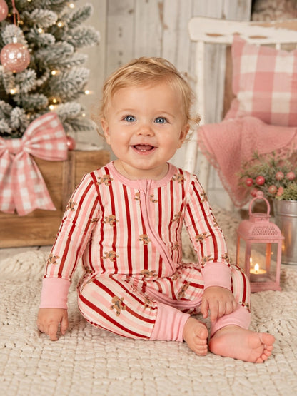 Smiling baby in red and pink striped pajamas sitting on a cozy rug, with a decorated Christmas tree in the background.