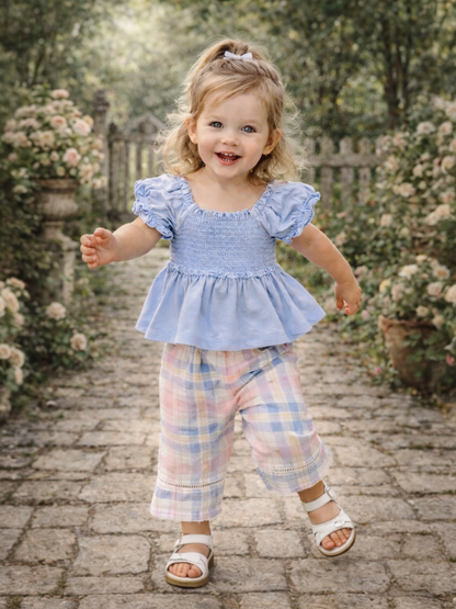 Smiling toddler in a blue top and plaid pants joyfully running along a stone pathway surrounded by flowers.