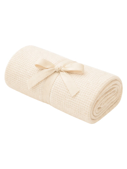 Rolled beige blanket tied with a ribbon, showcasing a textured fabric. Ideal for cozy home décor.
