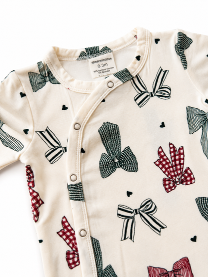 Infant onesie featuring a playful bow pattern in red and green on a cream background, labeled for size 0-3 months.
