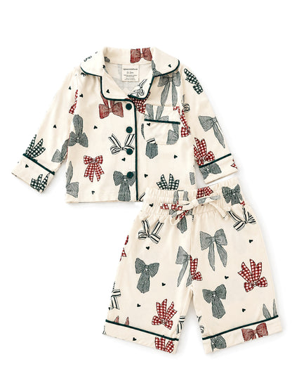 Children's pajama set featuring a patterned top and shorts with bows and heart designs in red and green on a cream background.