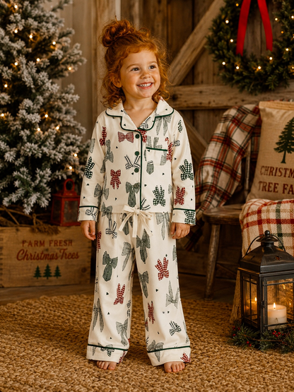 Smiling girl in festive pajamas with bows, standing by a Christmas tree and cozy decor.