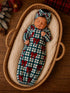 Newborn girl in a plaid outfit with red bows, peacefully sleeping in a cozy woven basket.