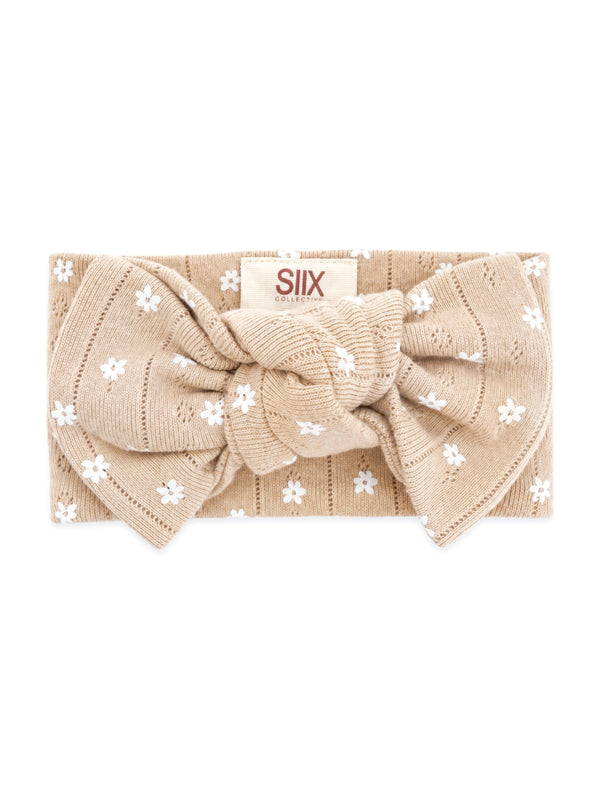 Beige headband with white floral patterns and a large bow, labeled "SIIX COLLECTIVE."